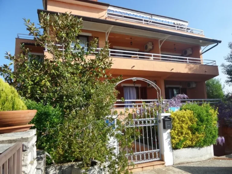 Kuća Apartmani Lina s ulice: narančasto pročelje, balkoni i ulazna vrata u zelenilu